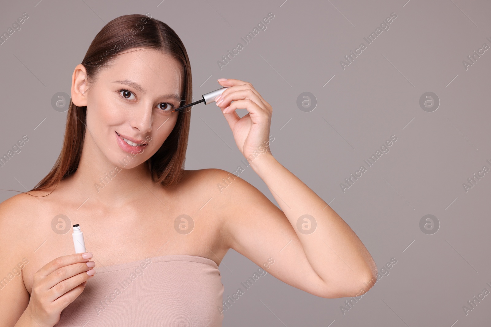 Photo of Beautiful woman applying serum onto eyelashes on grey background