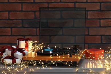 Photo of Turntable with vinyl record, fairy lights and Christmas gift boxes on grey table