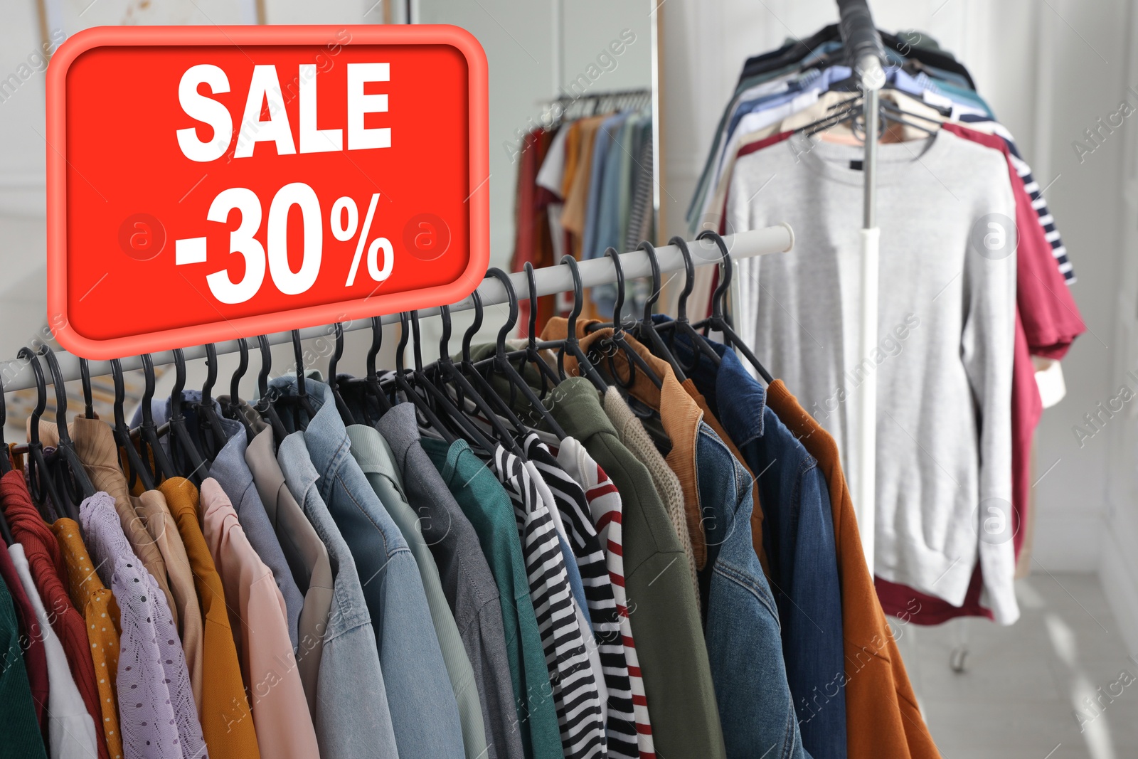 Image of Sale sign and rack with collection of stylish women's clothes in modern boutique