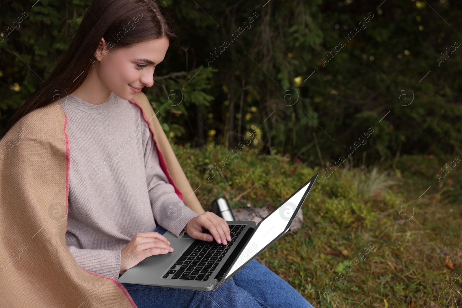 Photo of Young woman working on laptop in forest, space for text