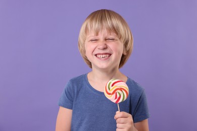 Photo of Happy little boy with colorful lollipop swirl on violet background