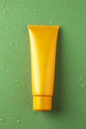 Moisturizing cream in tube on green background with water drops, top view