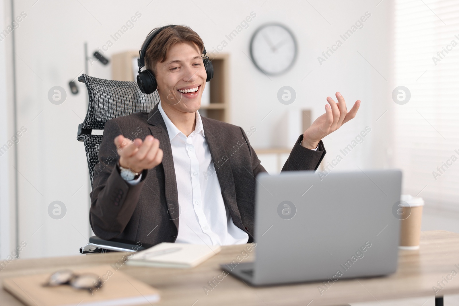 Photo of Man in headphones using video chat during webinar at wooden table in office