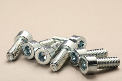 Many metal socket screws on beige background, closeup