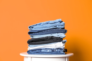 Photo of Stack of different jeans on table against color background