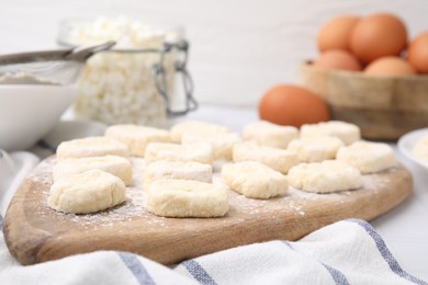 Photo of Making lazy dumplings. Wooden board with cut dough and flour on table, closeup