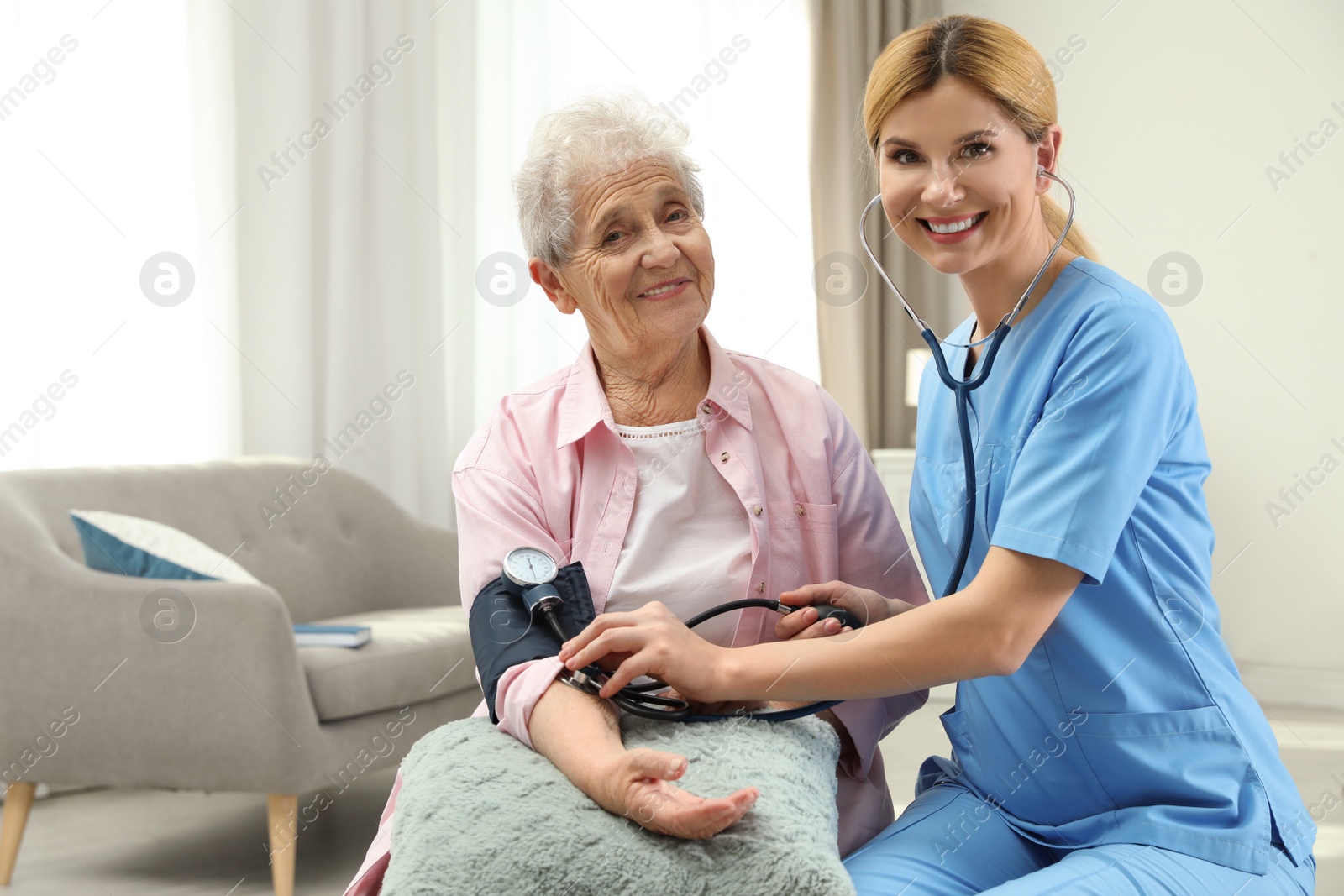 Photo of Nurse measuring blood pressure of elderly woman indoors. Assisting senior people