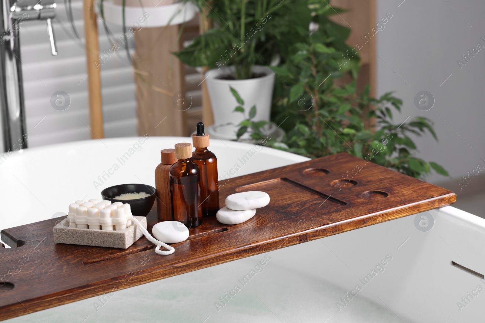 Photo of Wooden board with spa products on bath tub in bathroom, space for text