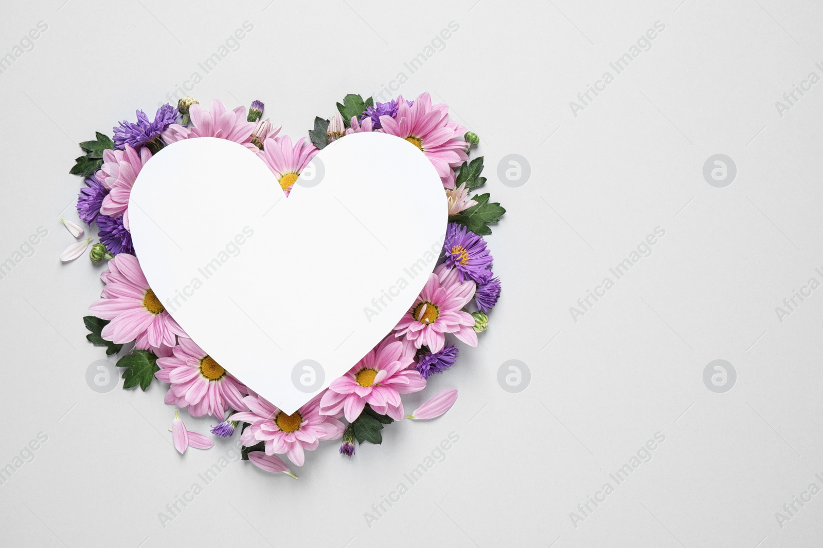 Photo of Beautiful chamomile flowers and heart shaped paper card on white background, top view with space for text