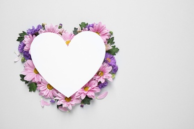 Beautiful chamomile flowers and heart shaped paper card on white background, top view with space for text