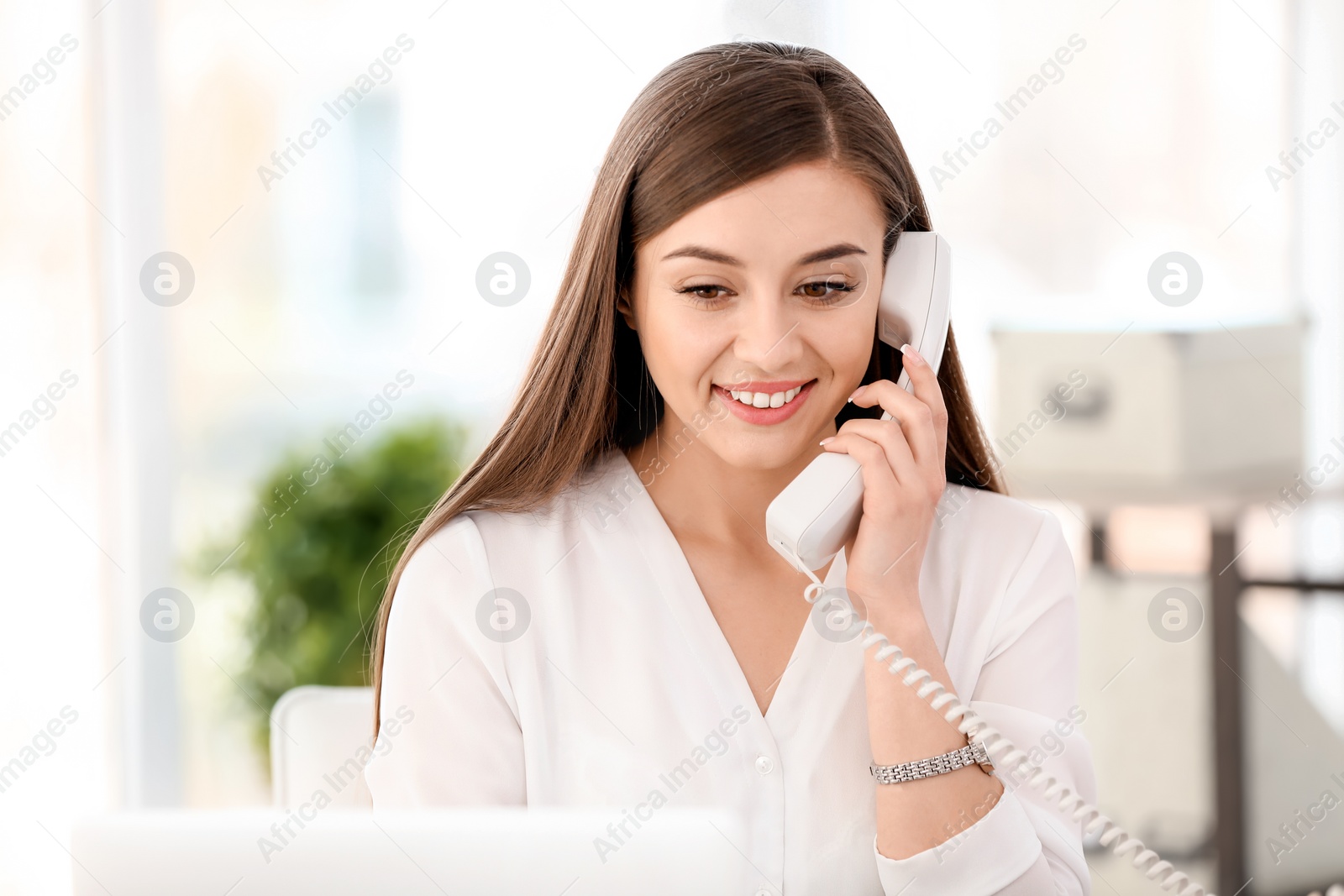 Photo of Young woman talking on phone at workplace