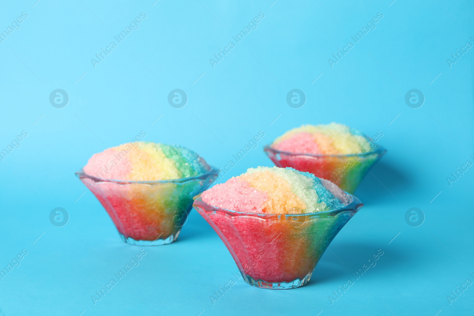 Photo of Rainbow shaving ice in glass dessert bowls on light blue background