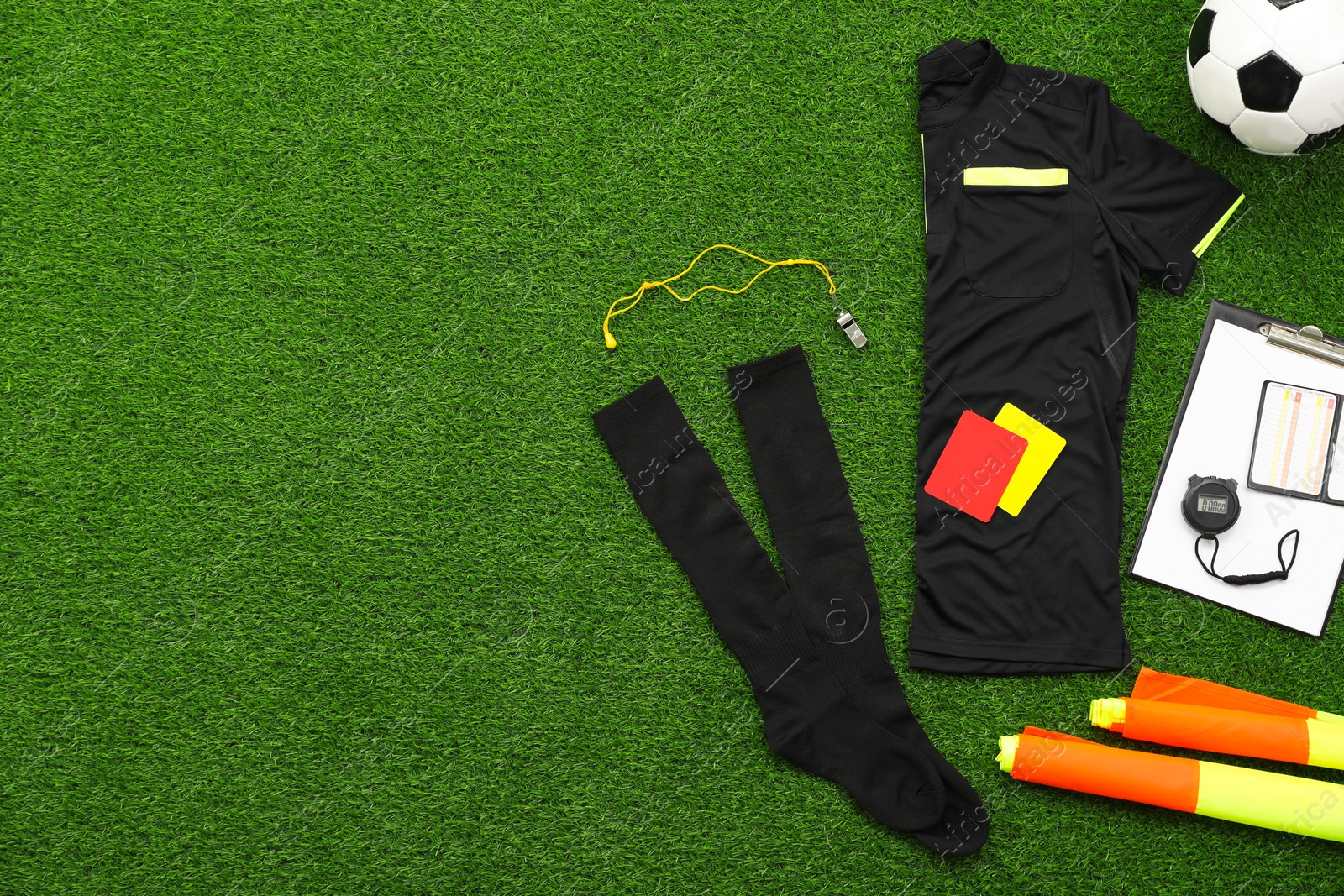 Photo of Uniform, soccer ball and other referee equipment on green grass, flat lay. Space for text