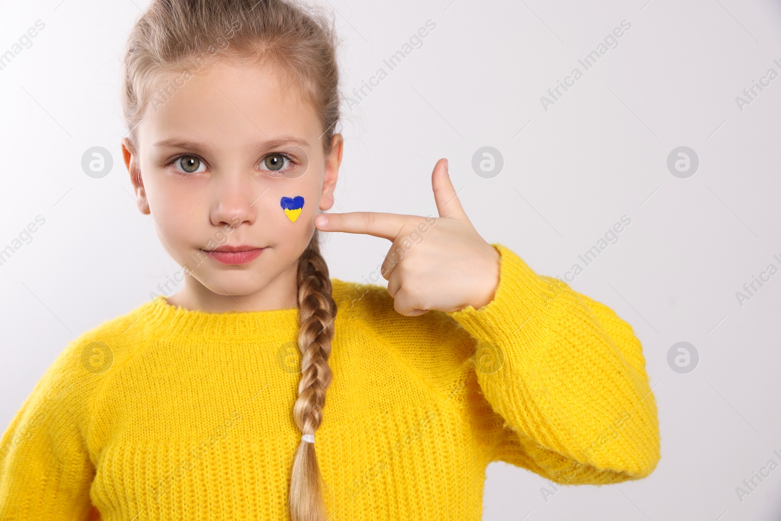 Photo of Little girl with drawing of Ukrainian flag on face against white background