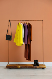 Rack with stylish women's clothes and boots near color wall