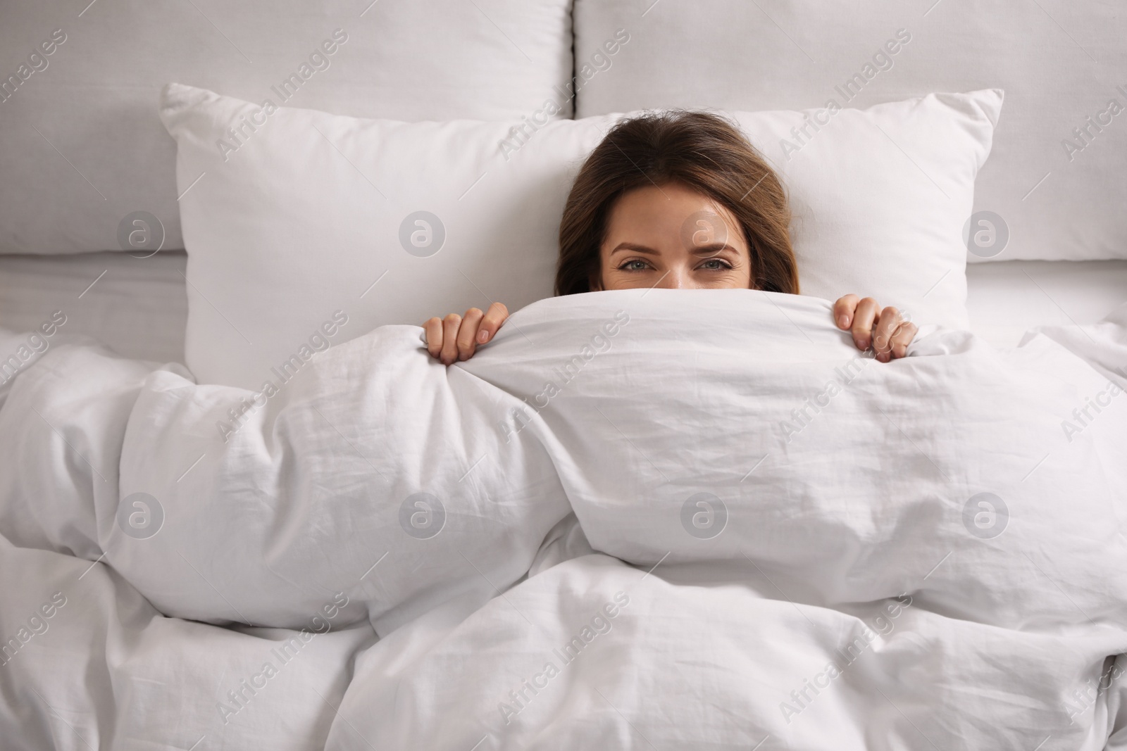 Photo of Woman hiding under warm white blanket in bed, above view