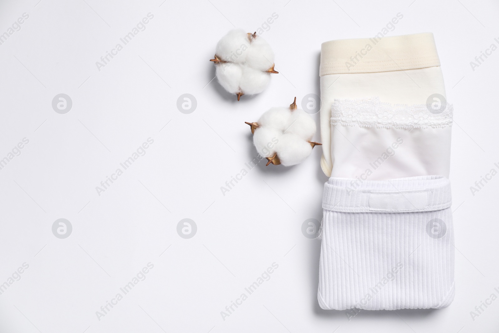 Photo of Stylish folded women's underwear and cotton flowers on white background, flat lay. Space for text