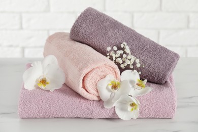 Photo of Rolled and folded towels with lilies on white table, closeup