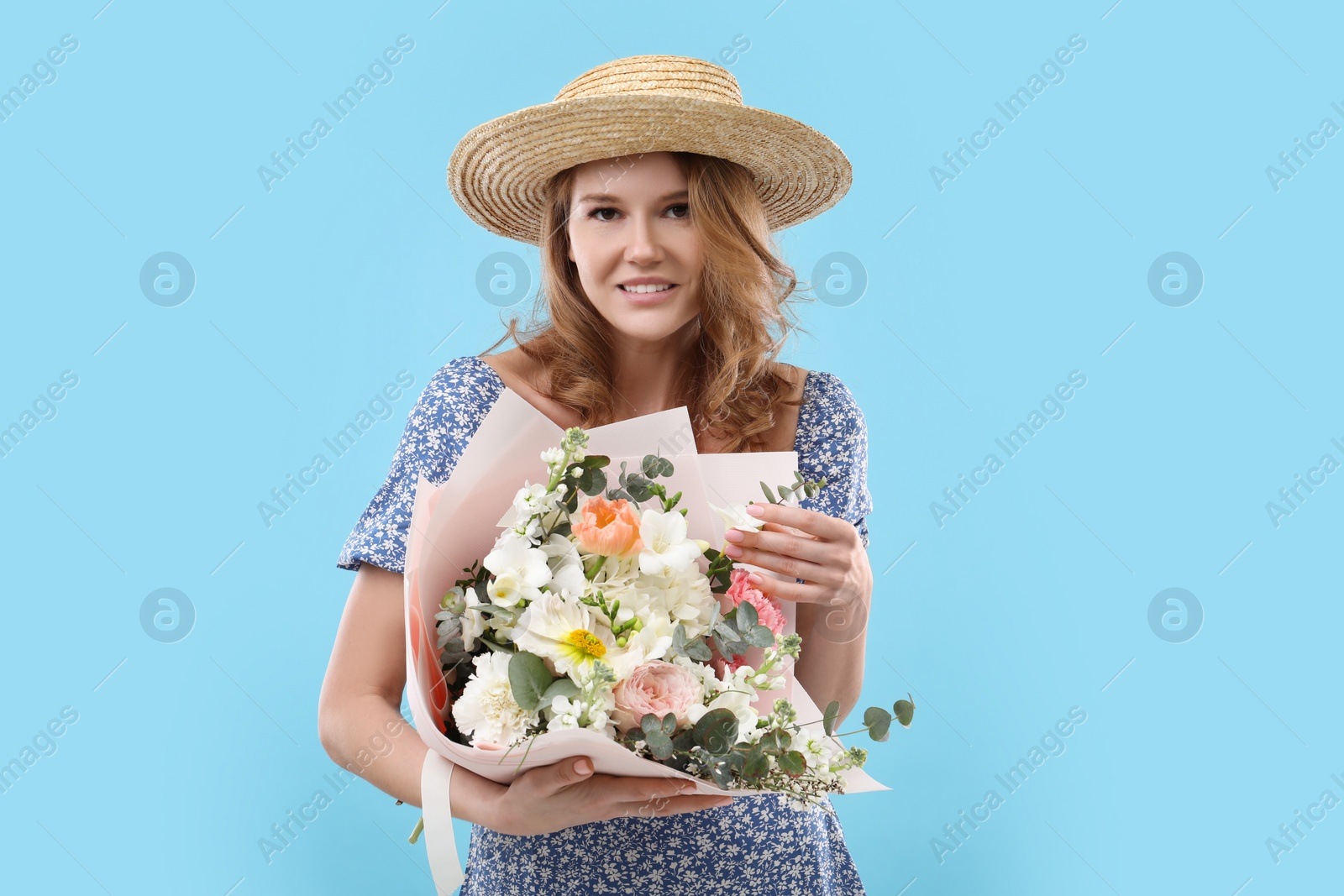 Photo of Beautiful woman in straw hat with bouquet of flowers on light blue background