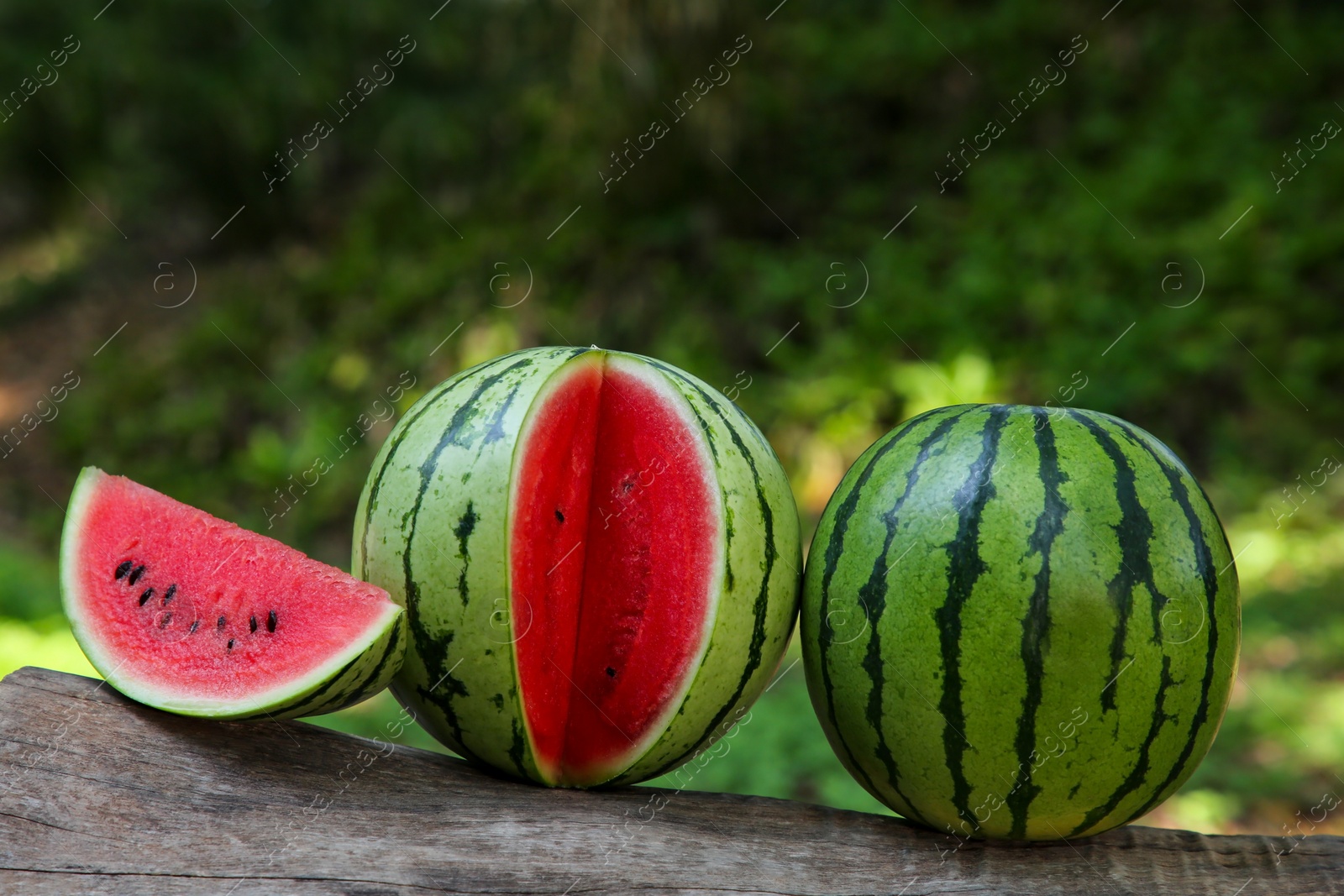 Photo of Delicious whole and cut watermelons on log outdoors