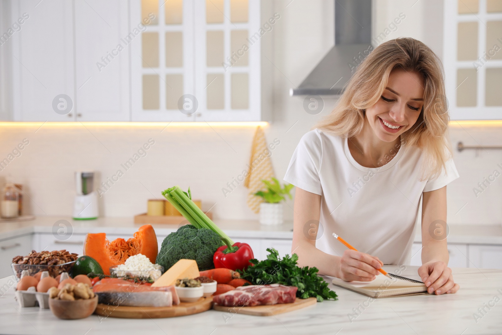 Photo of Woman with notebook and healthy food at white table in kitchen. Keto diet