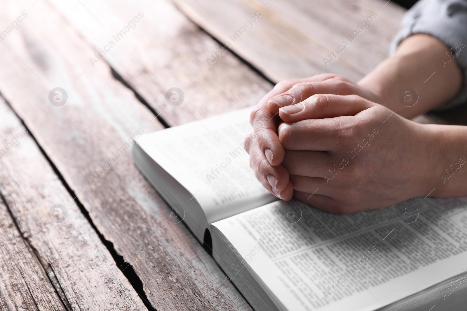 Photo of Religion. Christian woman praying over Bible at wooden table, closeup