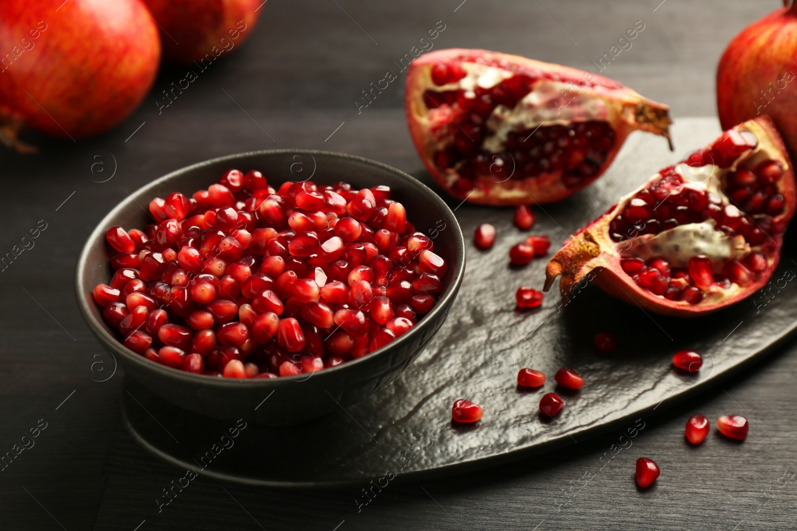 Photo of Tasty ripe pomegranates and grains on dark wooden table