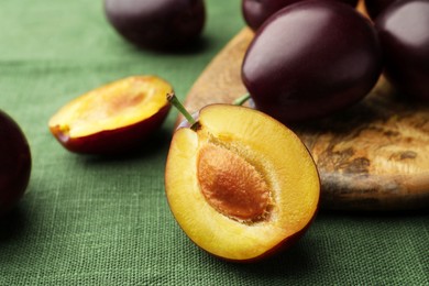 Photo of Many tasty ripe plums and wooden board on green fabric, closeup