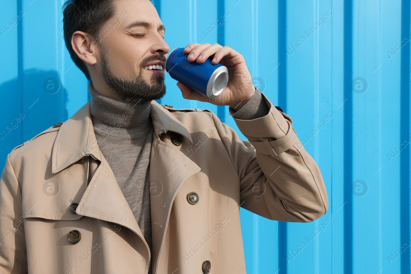 Photo of Handsome man drinking from tin can near light blue wall. Space for text