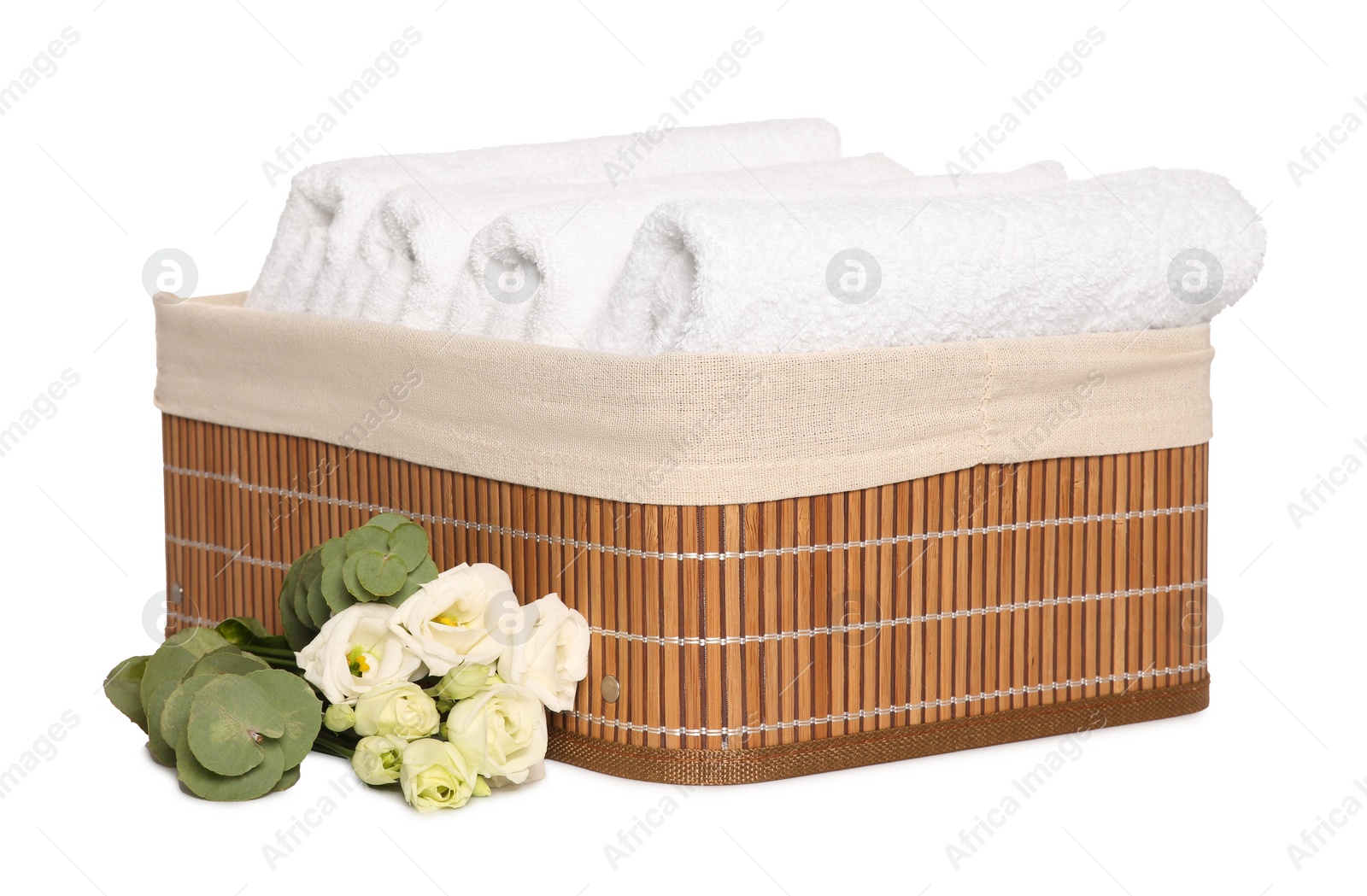 Photo of Wicker basket with folded soft terry towels, flowers and eucalyptus branch on white background