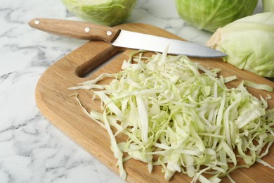 Photo of Chopped ripe cabbage and knife on white marble table, closeup