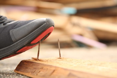 Photo of Careless worker stepping on nail in wooden plank outdoors, closeup. Space for text
