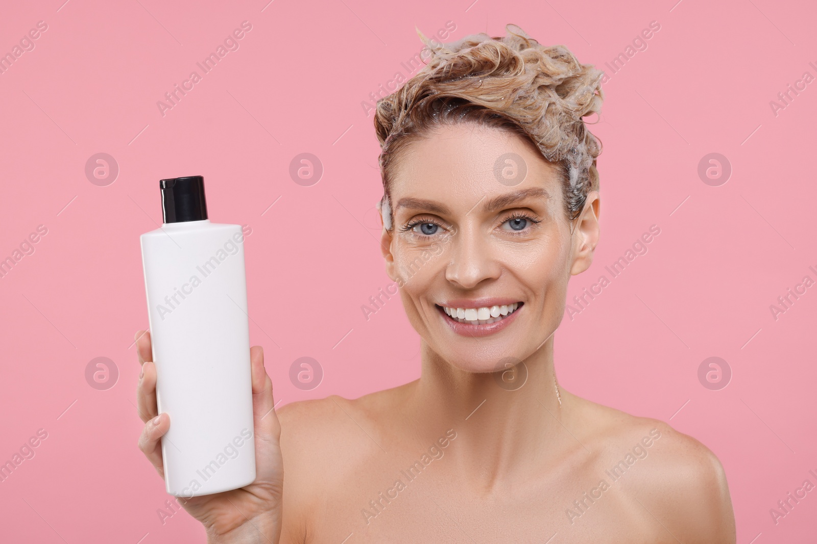 Photo of Beautiful happy woman with bottle washing hair on pink background