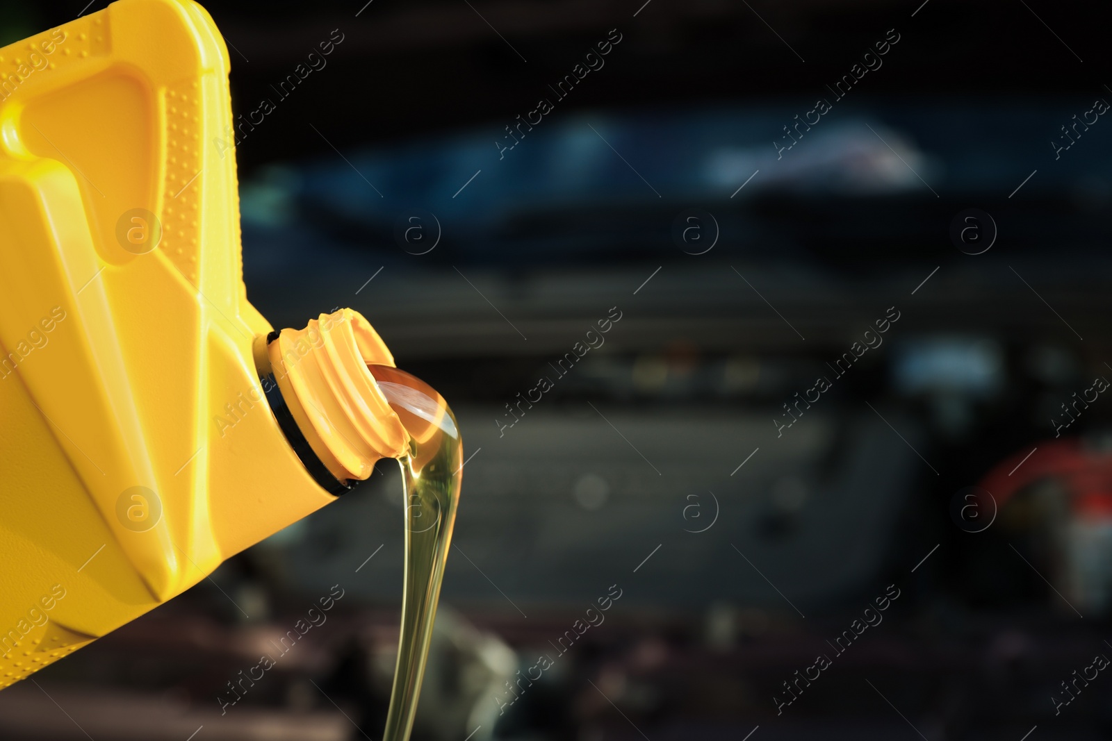 Photo of Pouring motor oil from yellow container on blurred background, closeup. Space for text