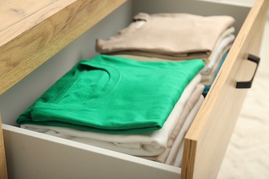 Stacks of different folded shirts in drawer indoors, closeup. Organizing clothes