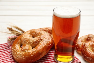 Photo of Glass of lager beer with tasty freshly baked pretzels on white table, closeup