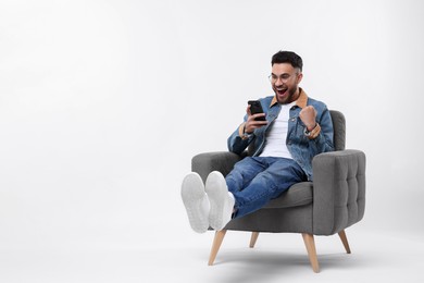 Photo of Happy man using smartphone in armchair on white background, space for text