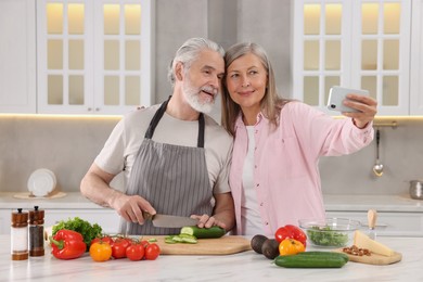Affectionate senior couple taking selfie while cooking together in kitchen