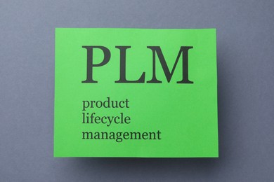 Green paper with abbreviation PLM (Product Lifecycle Management) on grey background, top view