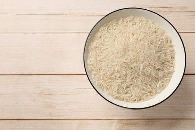 Photo of Raw basmati rice in bowl on white wooden table, top view. Space for text