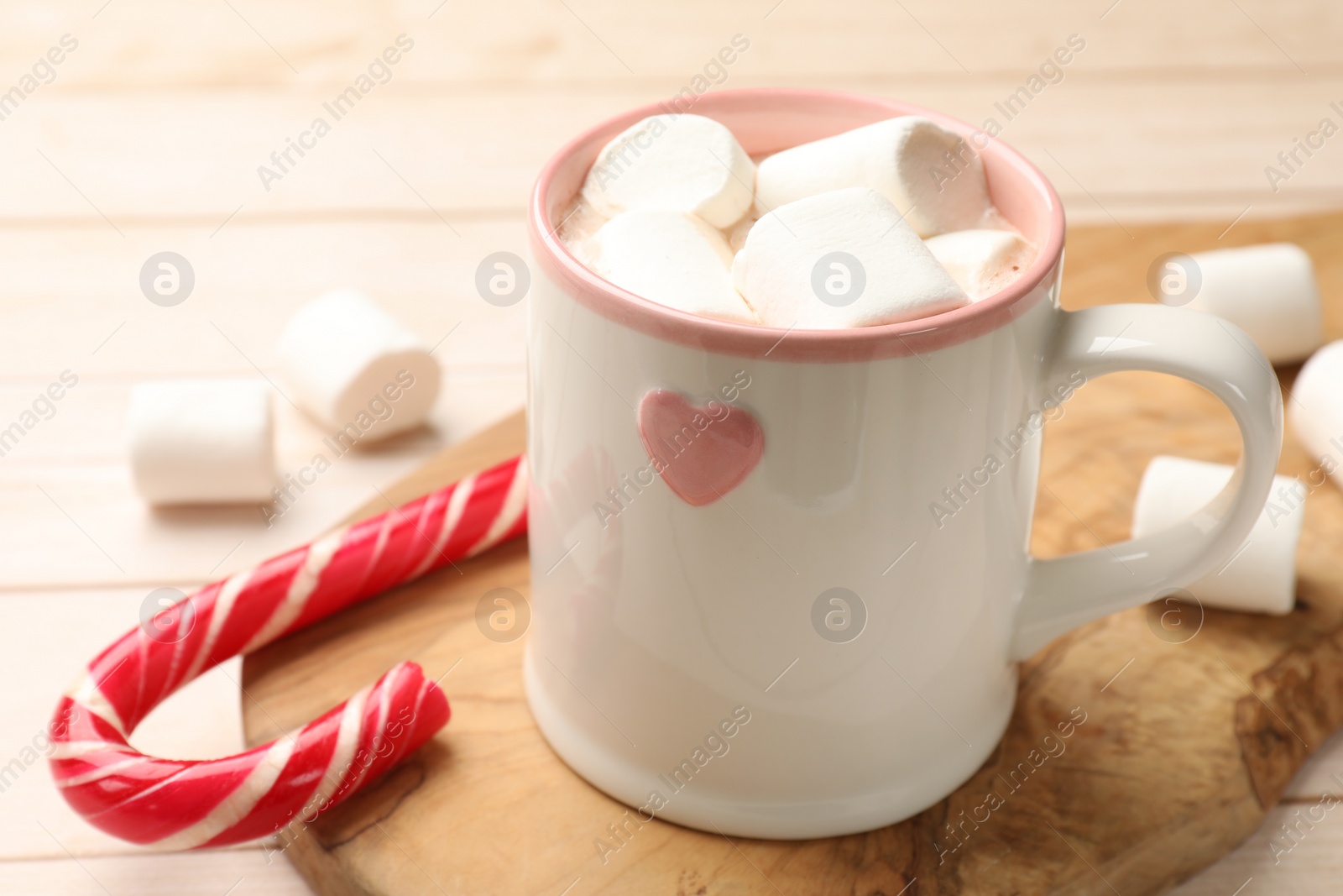 Photo of Tasty hot chocolate with marshmallows and candy cane on light wooden table, closeup