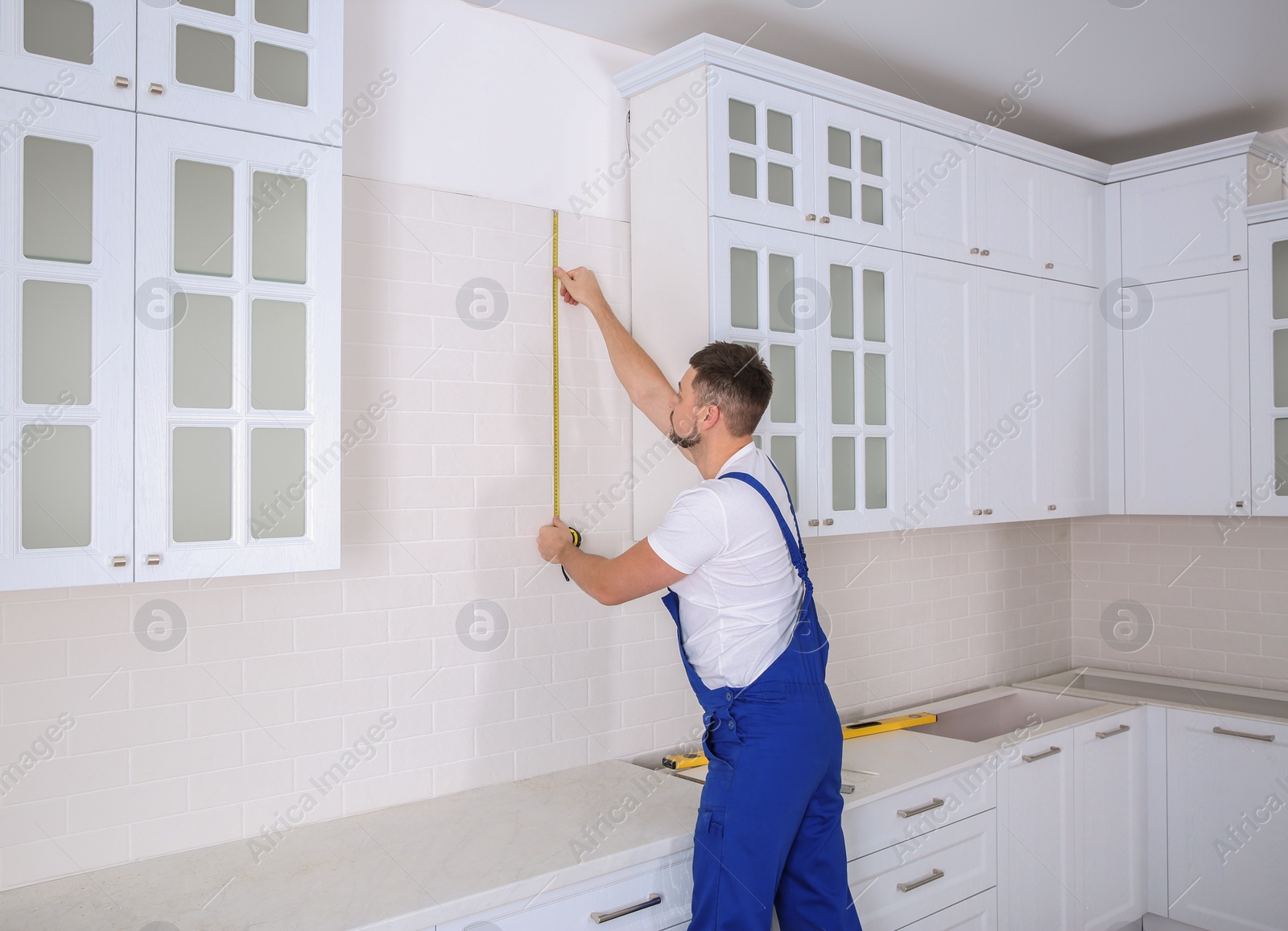 Photo of Worker using measuring tape while installing new furniture in kitchen