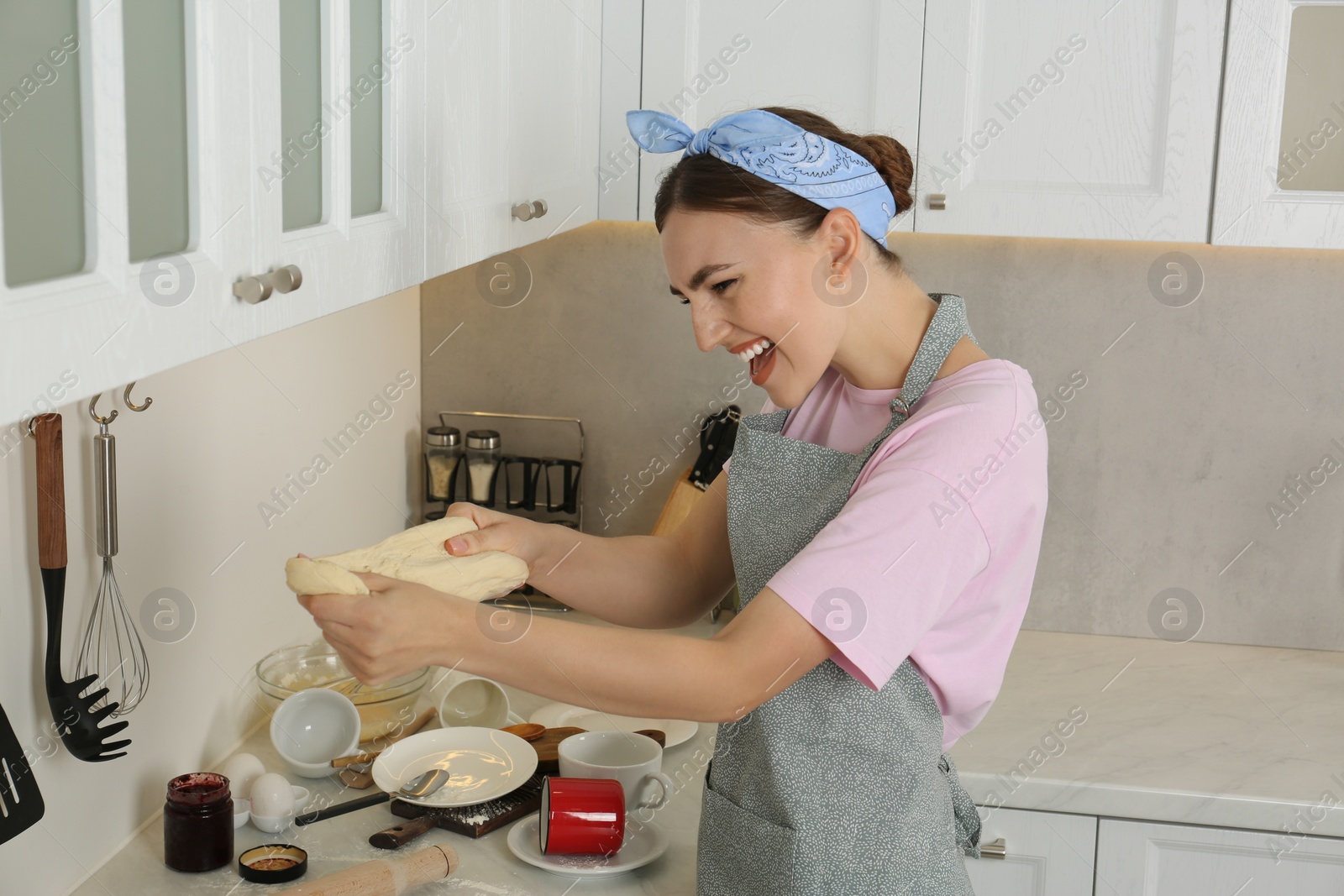 Photo of Emotional woman cooking in kitchen. Many dishware and utensils on messy countertop