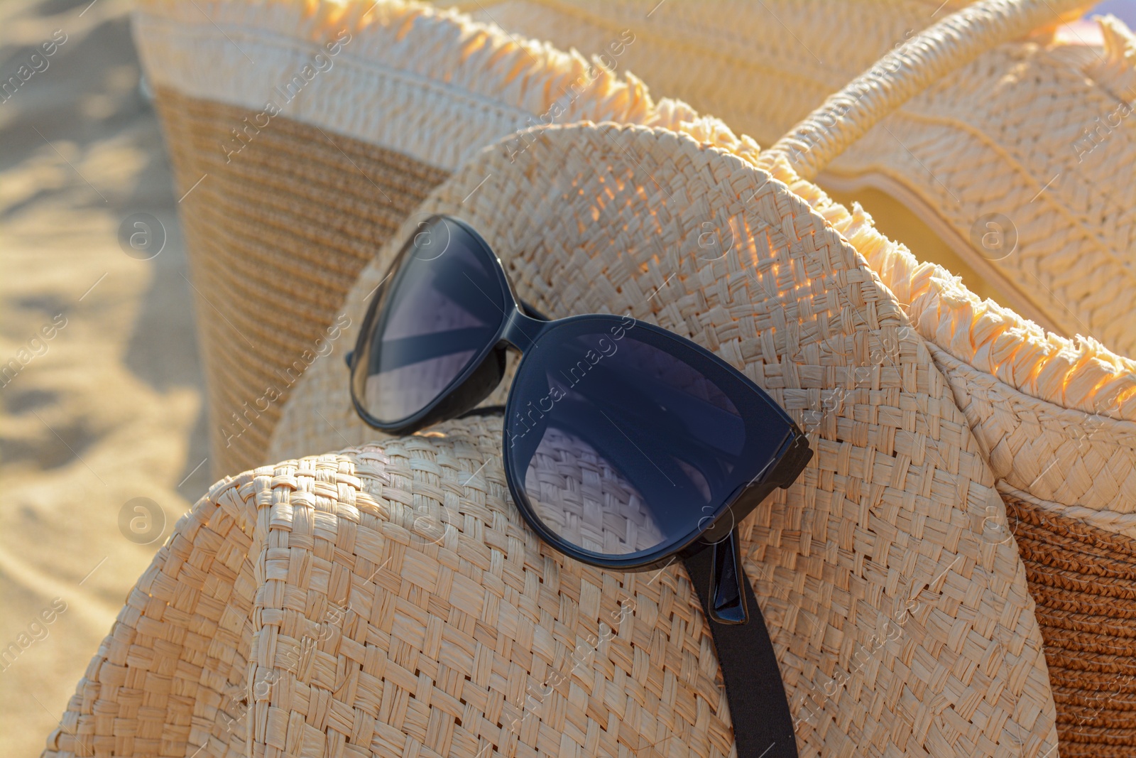 Photo of Hat and bag with beautiful sunglasses on sandy beach, closeup