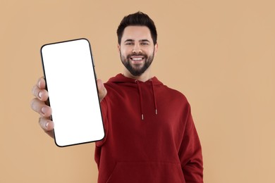 Happy man holding smartphone with empty screen on beige background