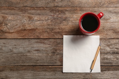 Clean napkin, cup of coffee and pen on wooden background, top view with space for text