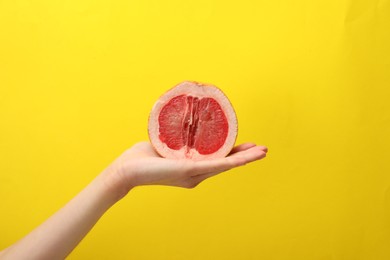 Photo of Woman holding half of grapefruit on yellow background, closeup. Sex concept