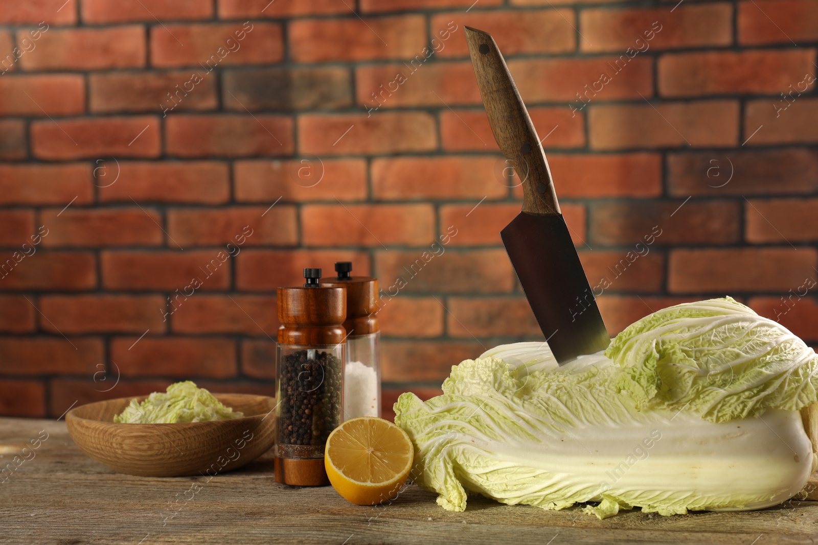 Photo of Fresh Chinese cabbage, knife, spices and lemon on wooden table