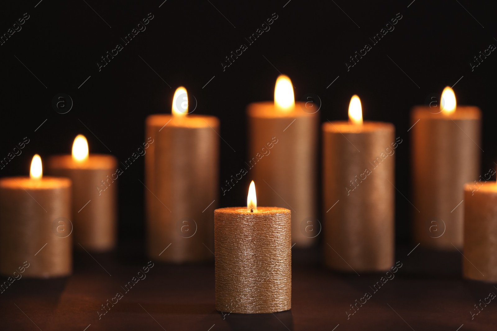 Photo of Burning gold candles on table against black background, space for text