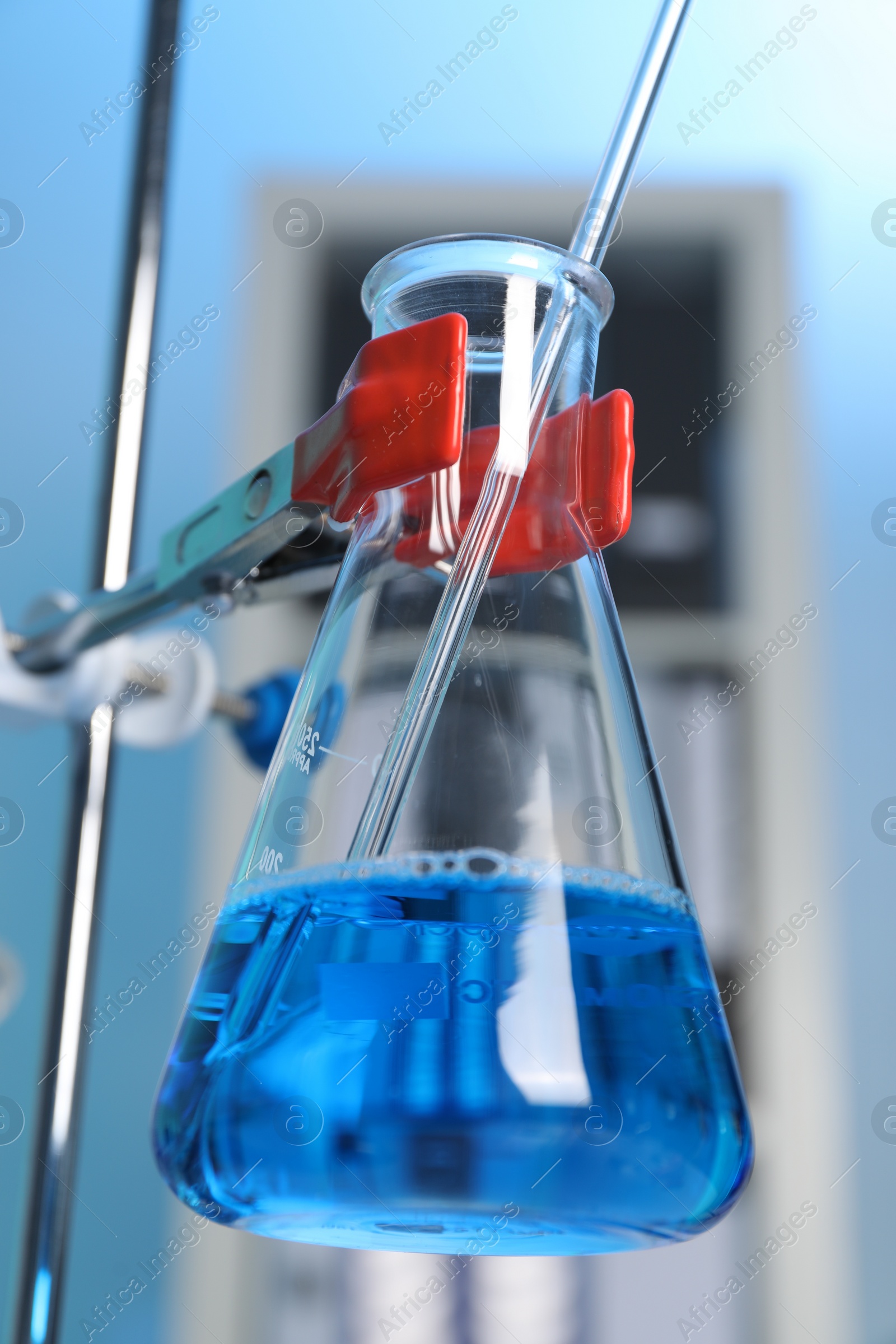 Photo of Laboratory analysis. Dripping blue liquid into flask on stand indoors, closeup